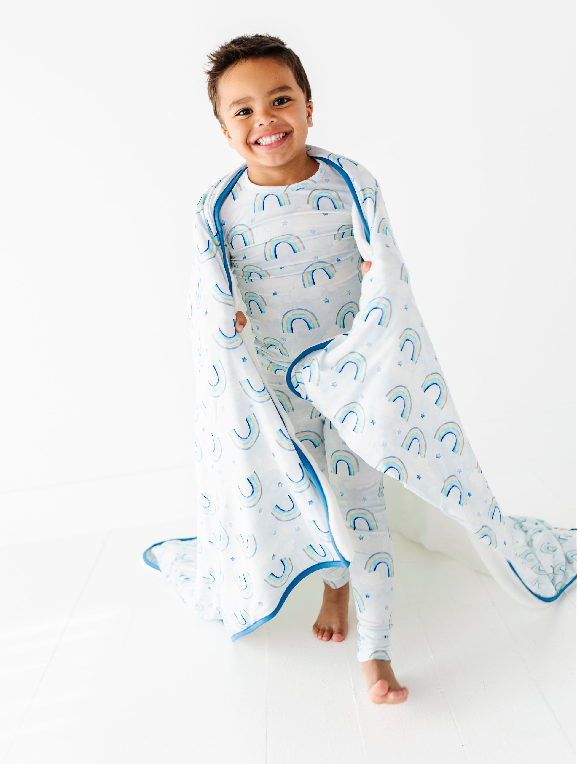 Child wrapped in a bamboo plush blanket featuring watercolor pastel rainbows on a white background