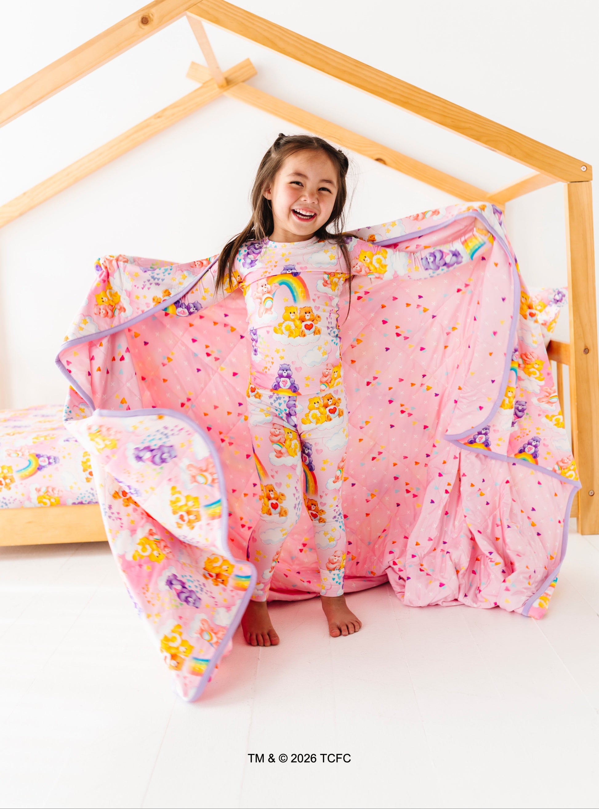 Child playing with a colorful comforter on a wooden frame bed.