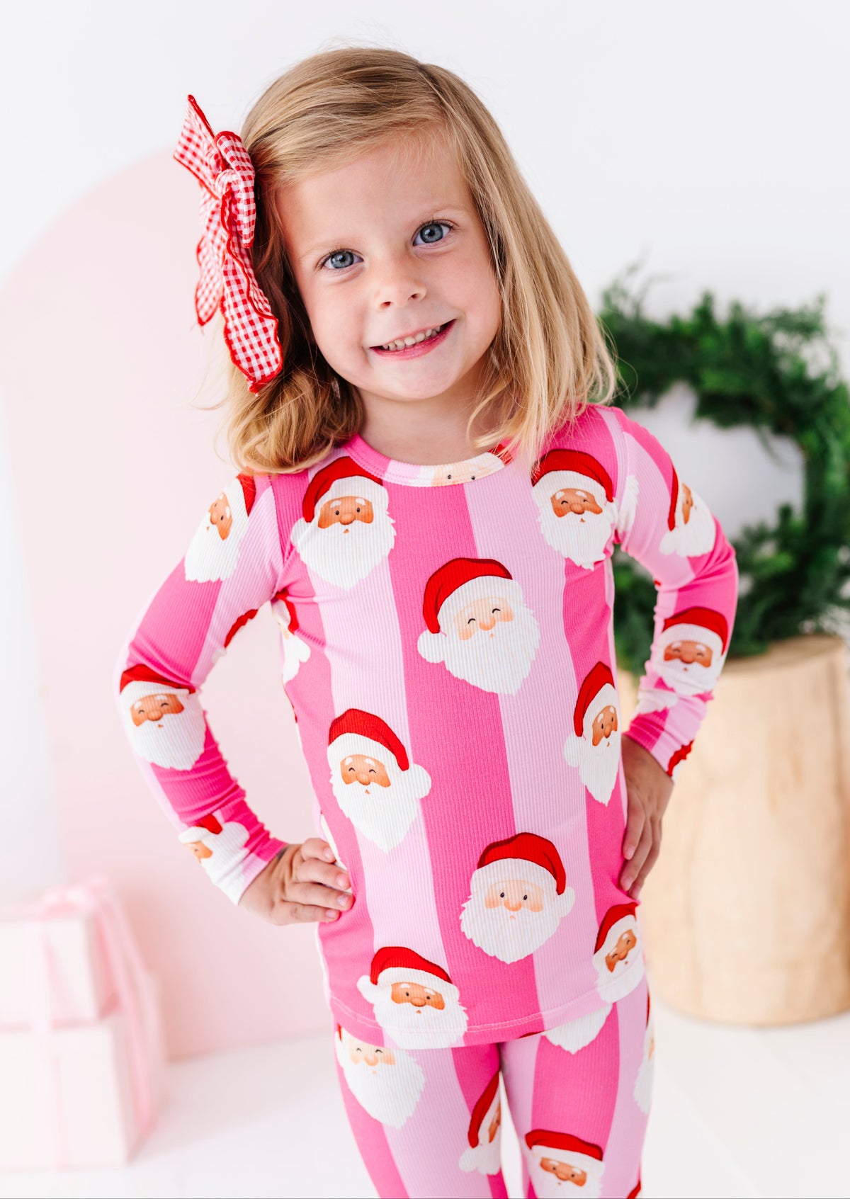 A young blonde girl wearing pink stripe ribbed bamboo pajamas featuring various Santa faces