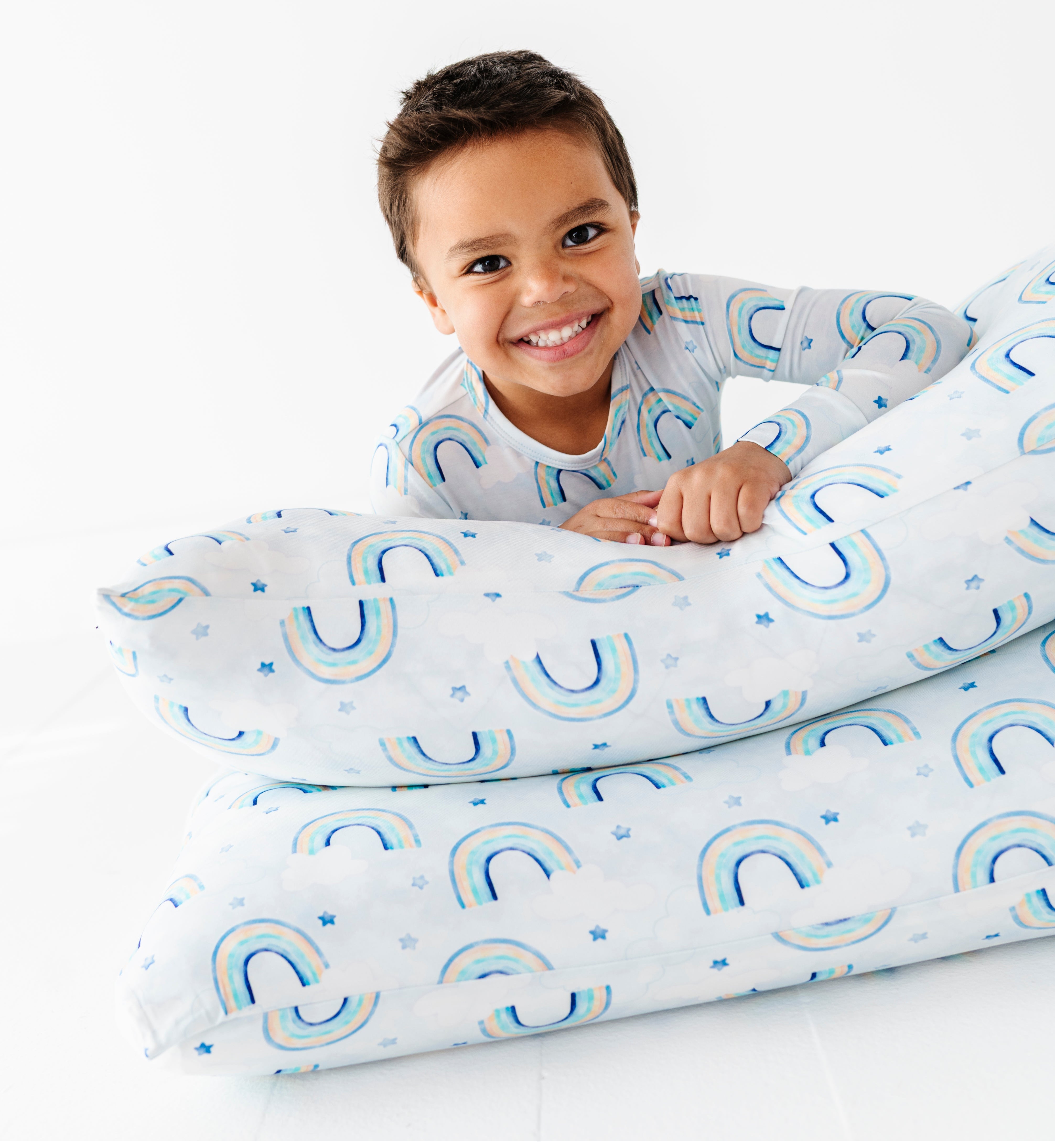 Little boy in bamboo watercolor rainbow pajamas lounging on matching watercolor rainbow pillowcases 