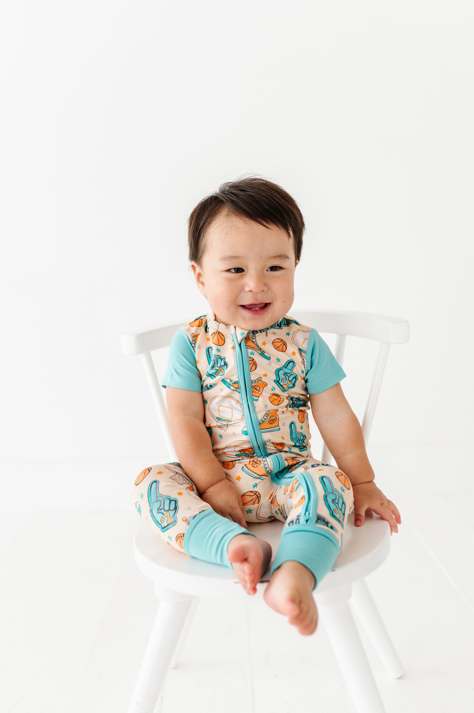 Child wearing a colorful bamboo outfit with a sports pattern sitting on a white chair.