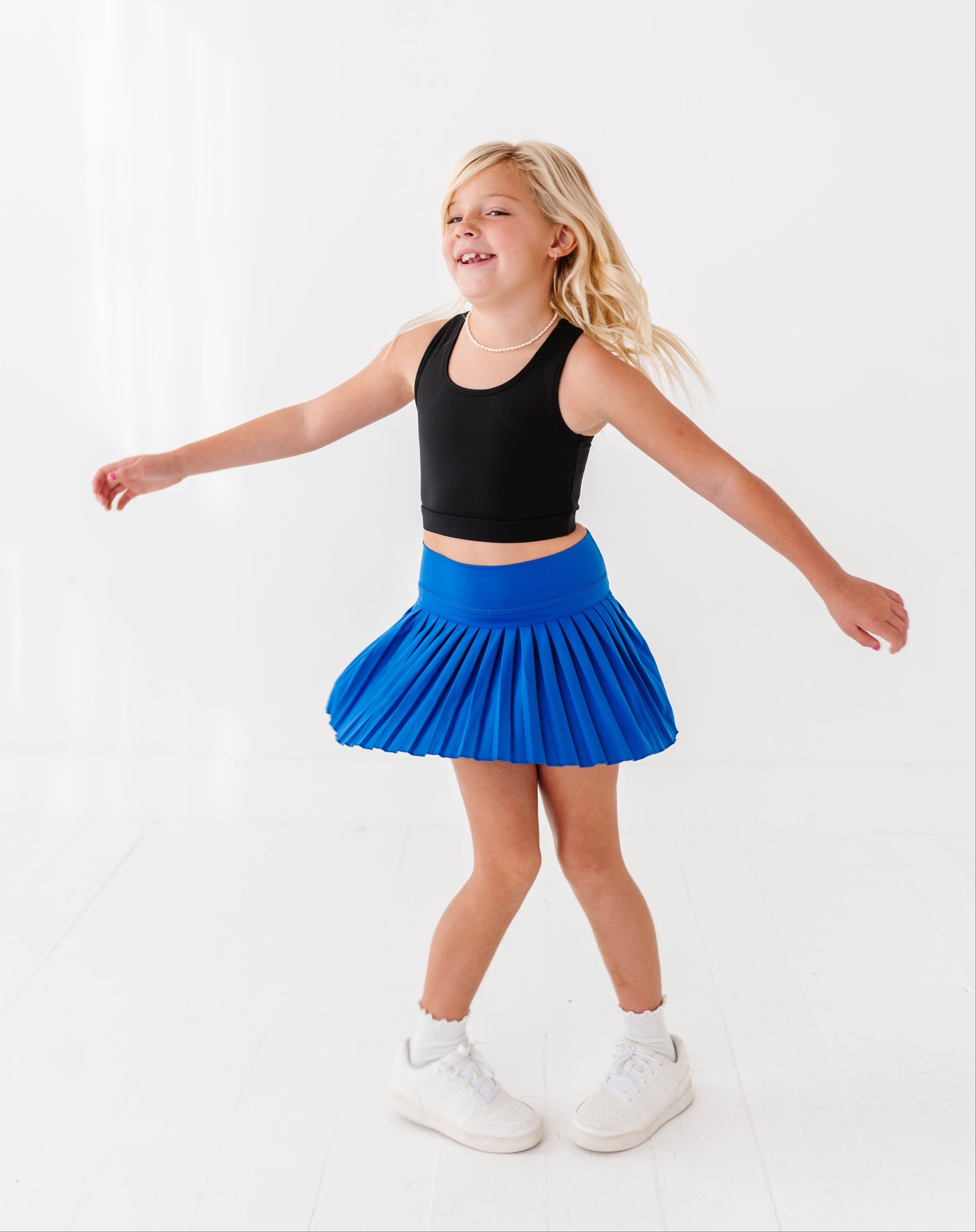 Young girl in a black top and blue active skort standing on a white background