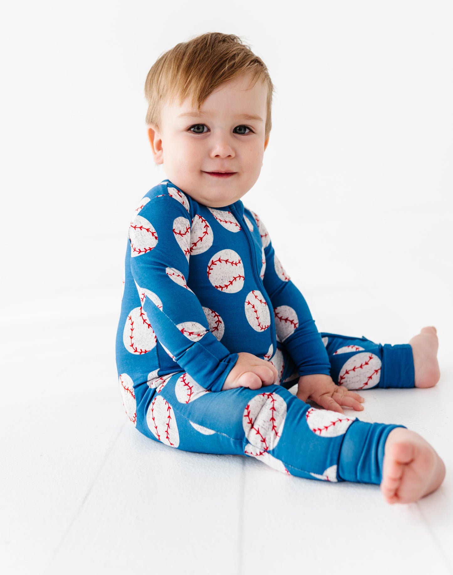 Baby wearing a blue bamboo convertible romper with baseball pattern on a white background