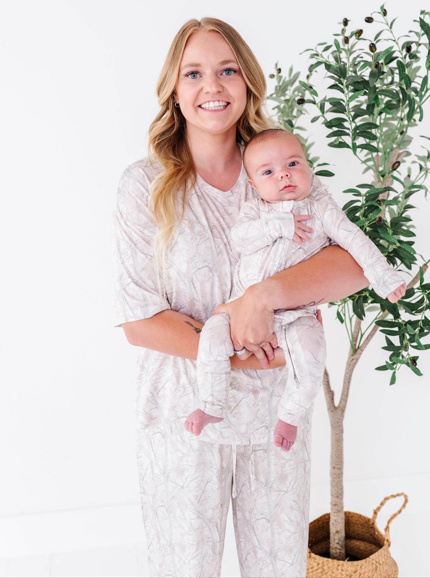 Woman holding a baby in matching pajamas with a plant in the background