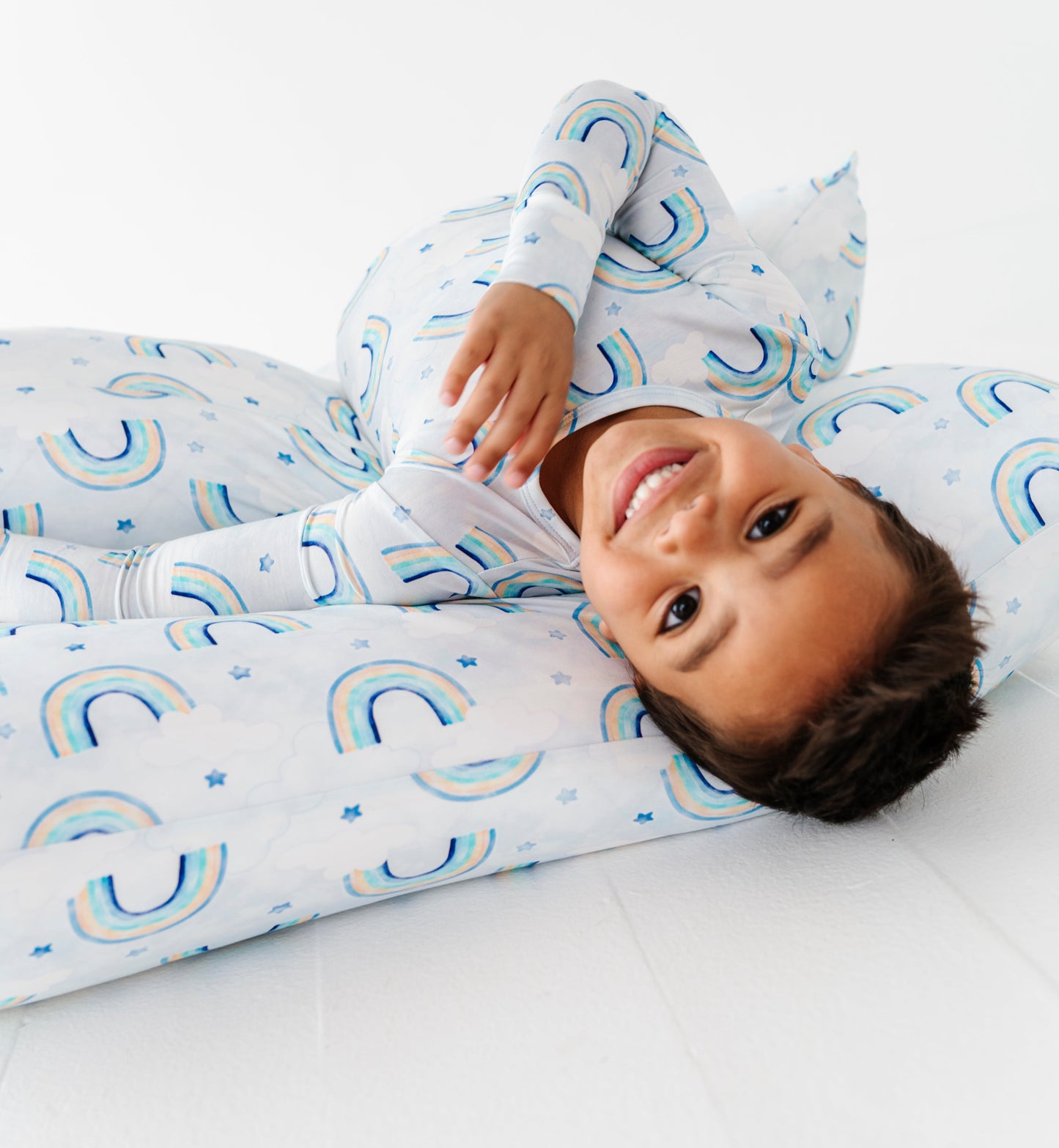 Child wearing a bamboo two-piece pajama set with blue watercolor rainbows on a white background