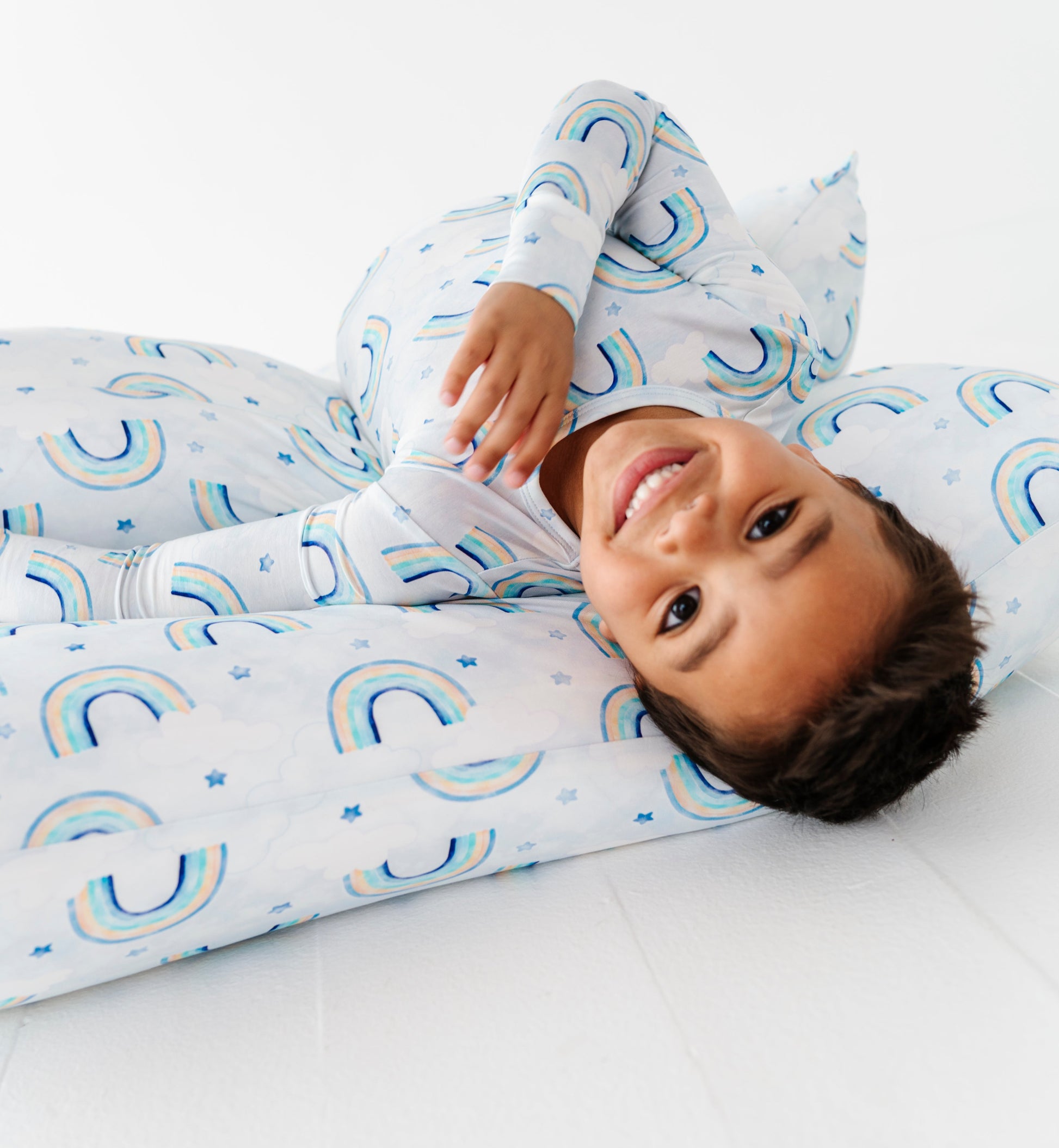 Child wearing a bamboo two-piece pajama set with blue watercolor rainbows on a white background