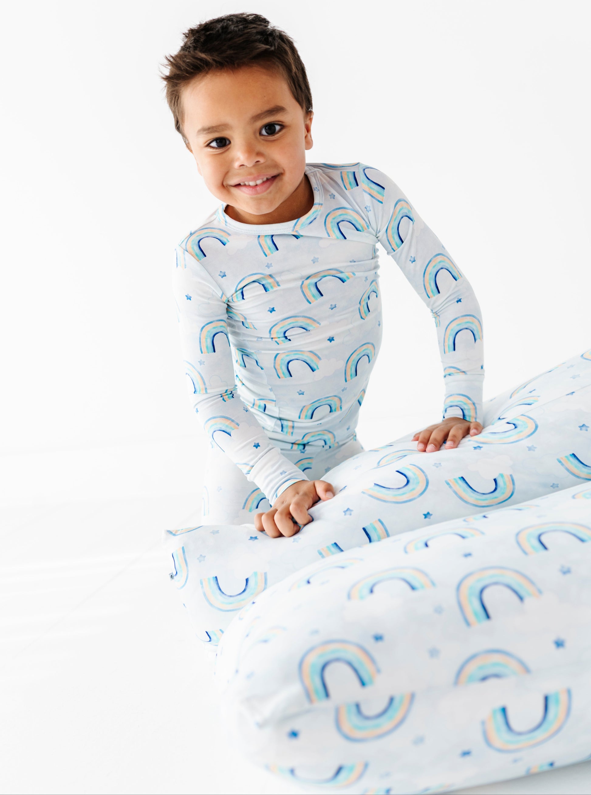 Child wearing a long-sleeve bamboo shirt and pants with watercolor rainbow patterns on a white background