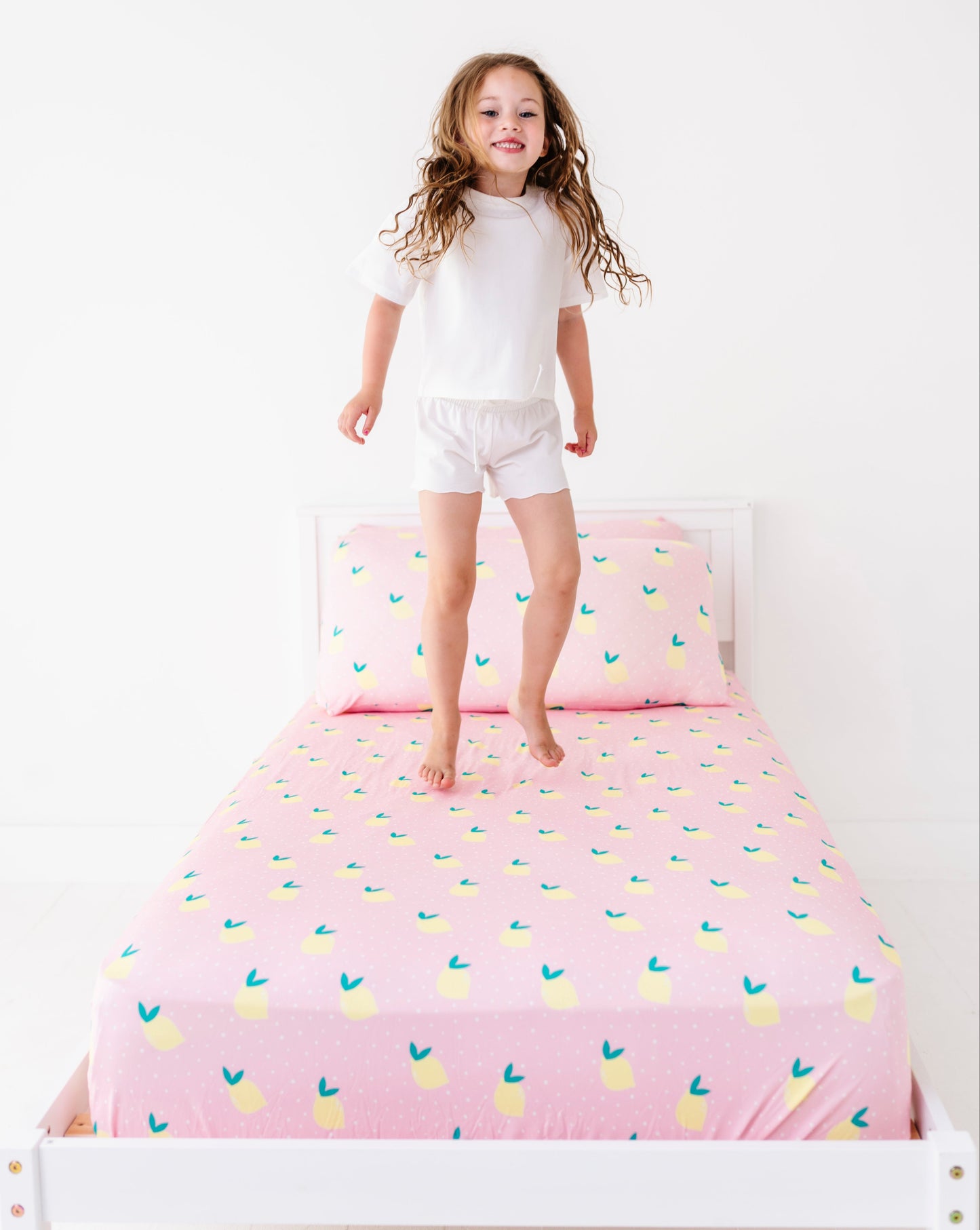 Child standing on a bed with pink bedding featuring lemon patterns