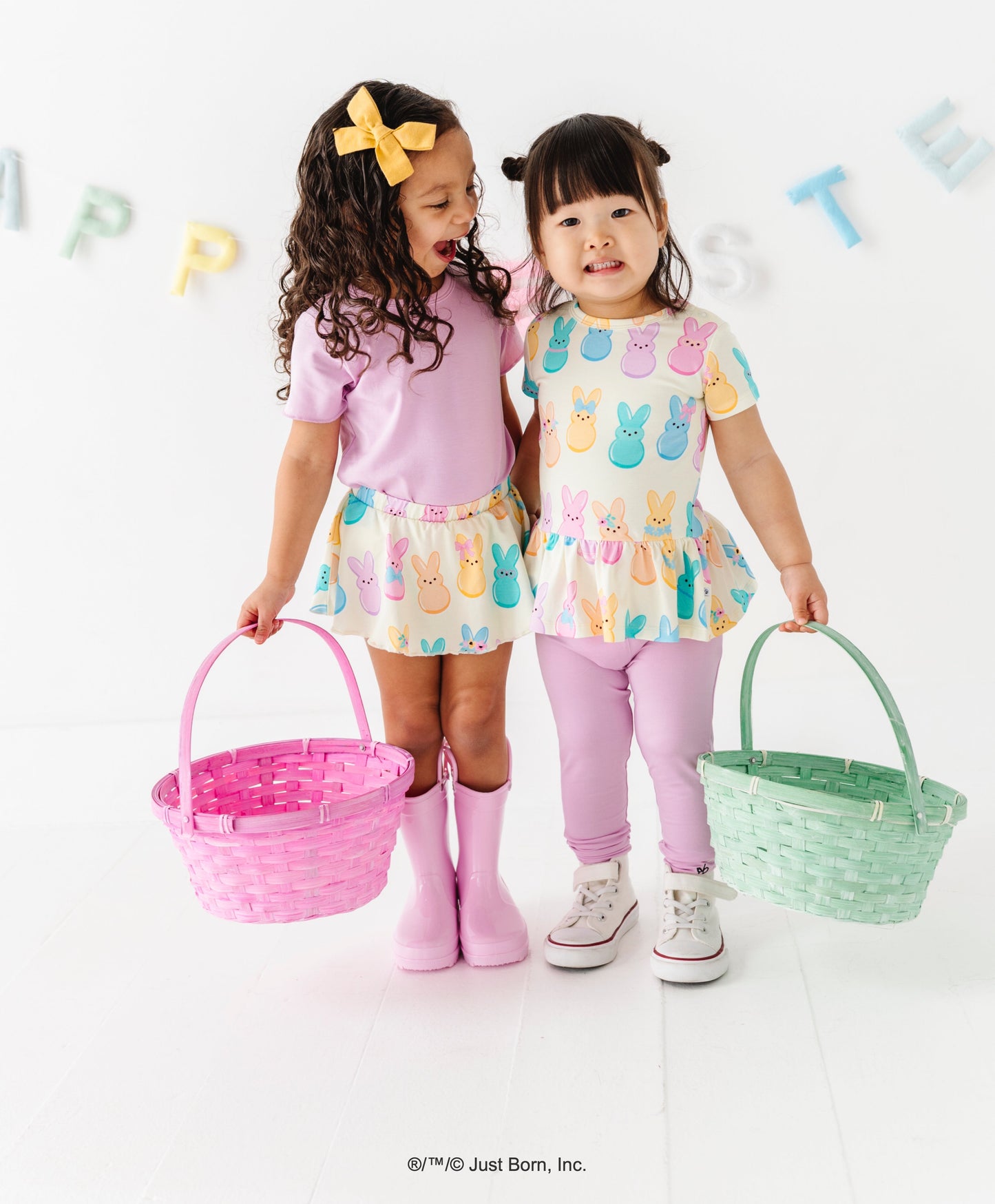 Two young girls in pastel PEEPS® outfits holding Easter baskets against a white background.
