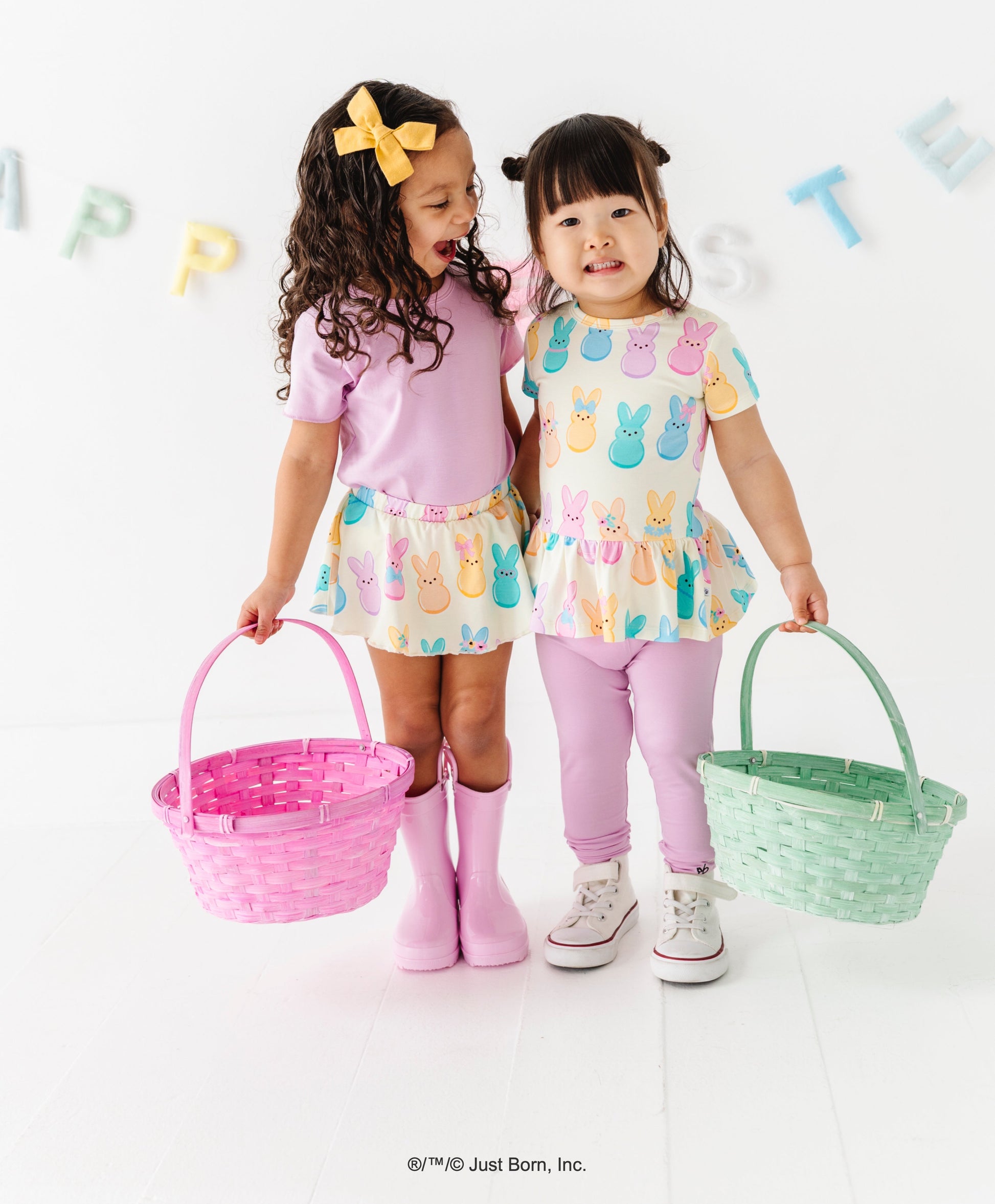 Two young girls in pastel PEEPS® outfits holding Easter baskets against a white background.
