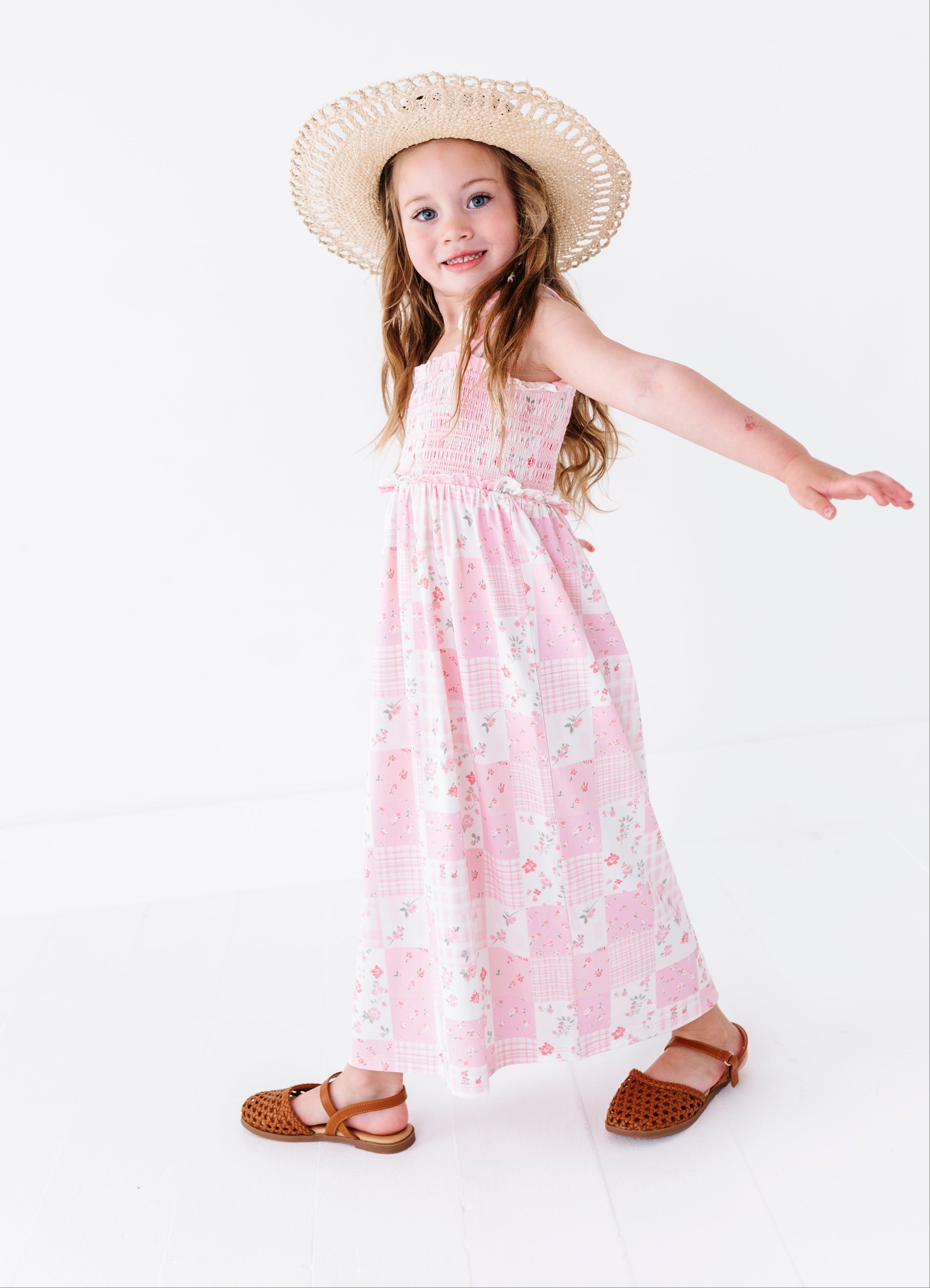 Young girl wearing a pink floral bamboo maxi dress and straw hat on a white background