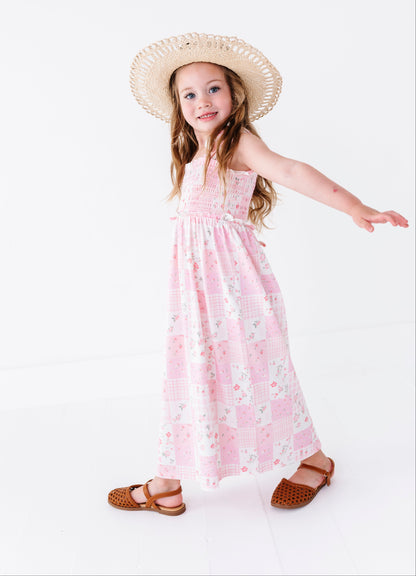 Young girl wearing a pink floral bamboo maxi dress and straw hat on a white background