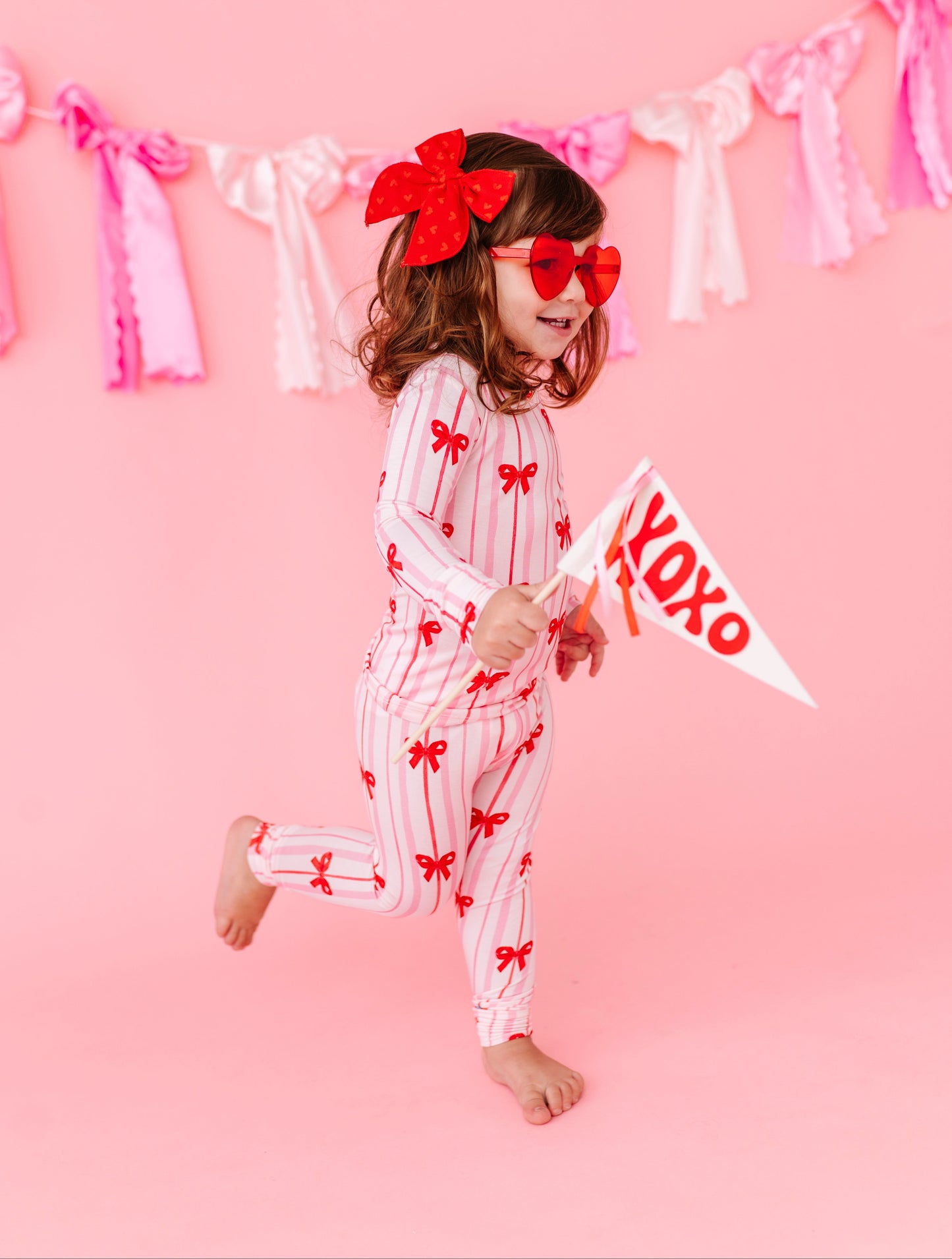 Child smiling in Ruby Ribbons two-piece bamboo pajamas on pink backdrop