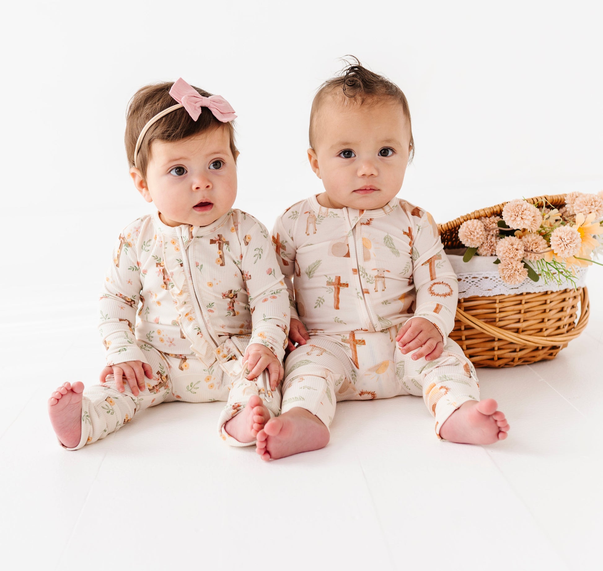 Two babies in matching Easter outfits sitting on a white floor with a basket and flowers.