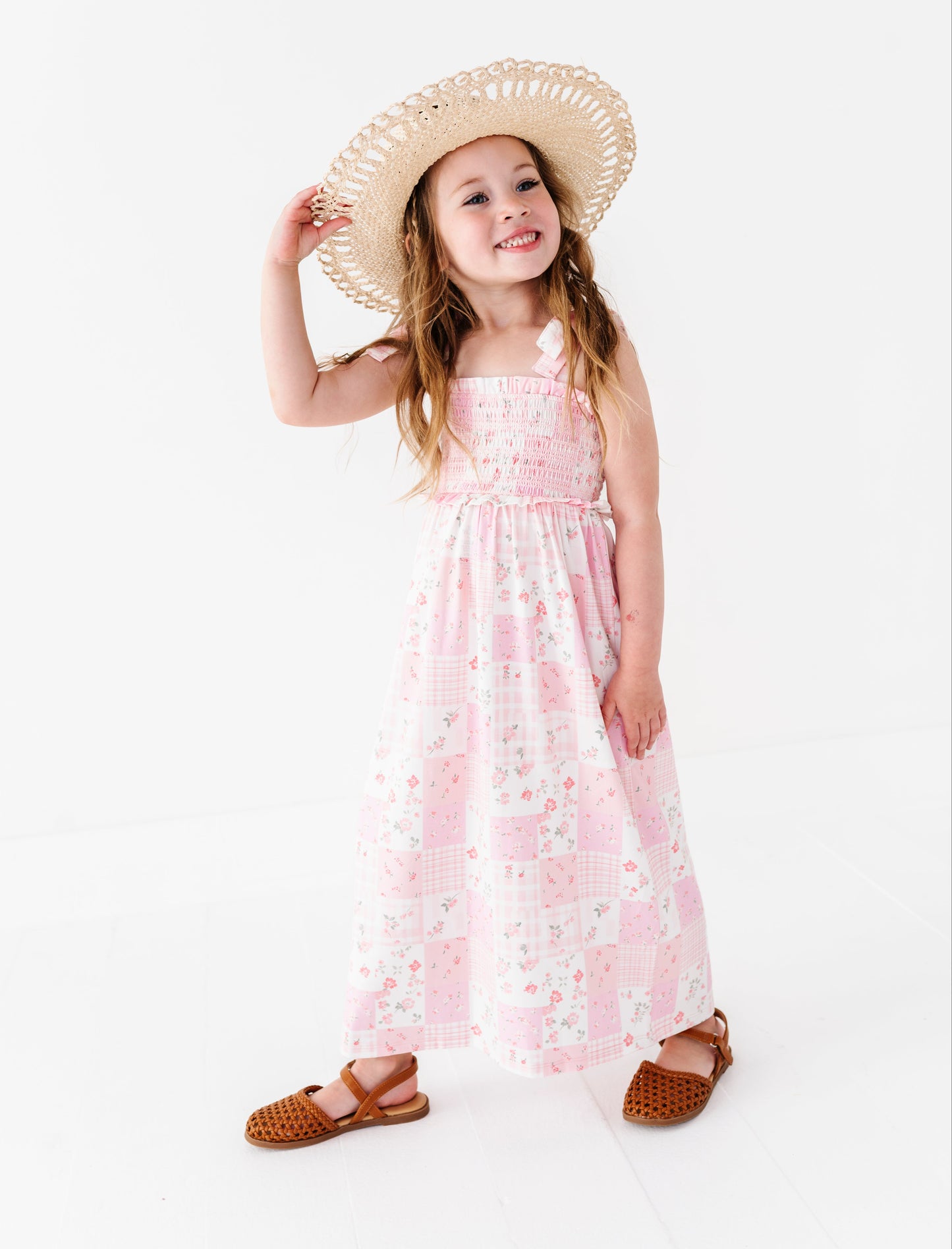 Young girl wearing a pink floral maxi dress and straw hat on a white background