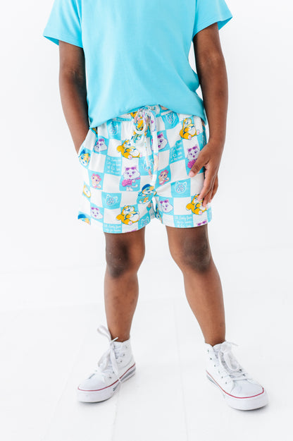 Young boy wearing a light blue bamboo blend shirt and colorful checkered 44 Cats shorts on a white background