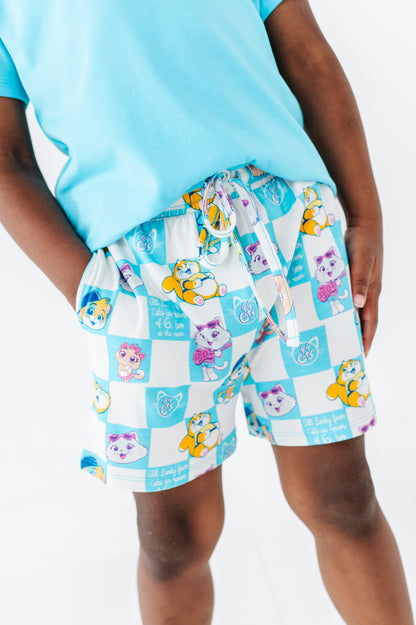 Little boy wearing a light blue bamboo bend shirt and checkered 44 Cats shorts on a white background