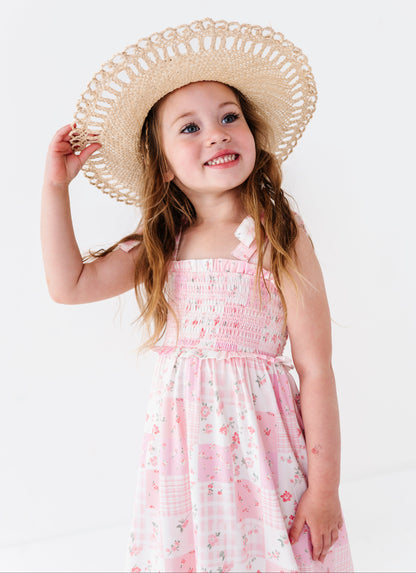 Young girl wearing a pink bamboo floral maxi dress and straw hat on a white background