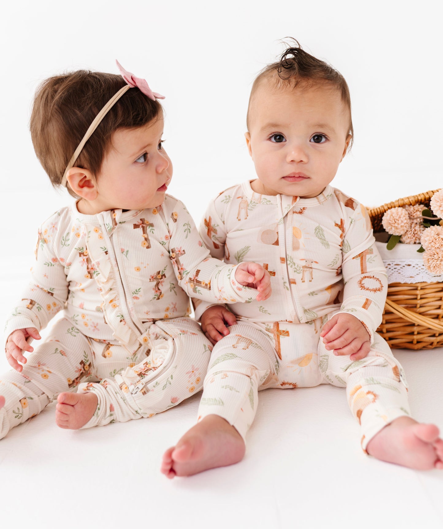 Two babies wearing coordinating Easter pajamas with a floral pattern on a white background.