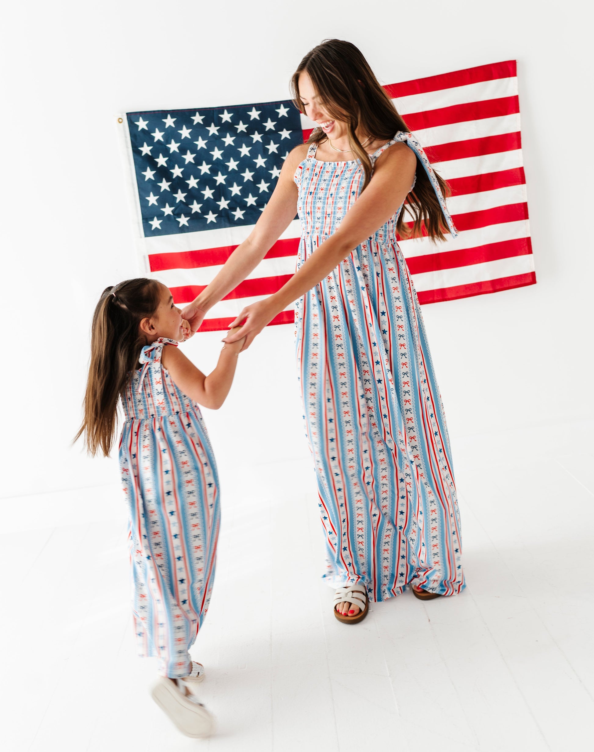 Mom and daughter in matching striped bamboo-cotton maxi dresses standing in front of an American flag.