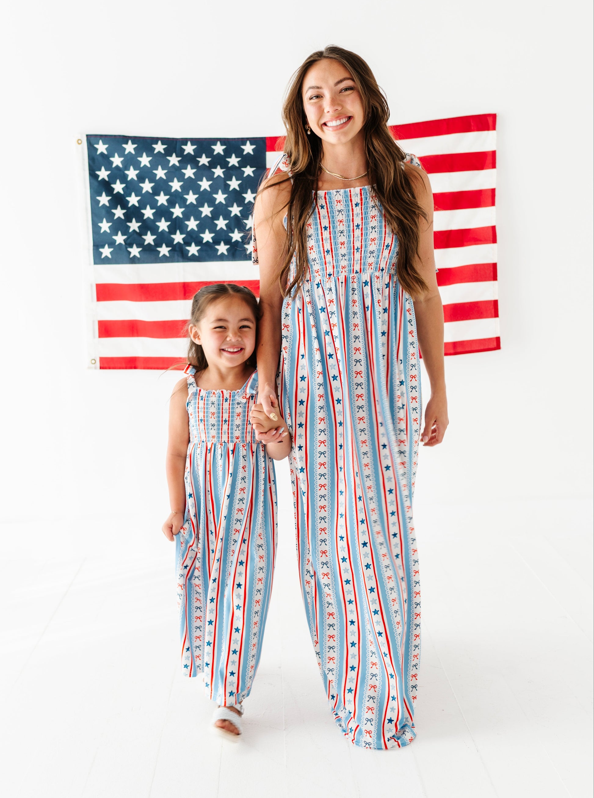 Mom and daughter wearing matching red, white, and blue striped bamboo-cotton maxi dresses in front of an American flag.
