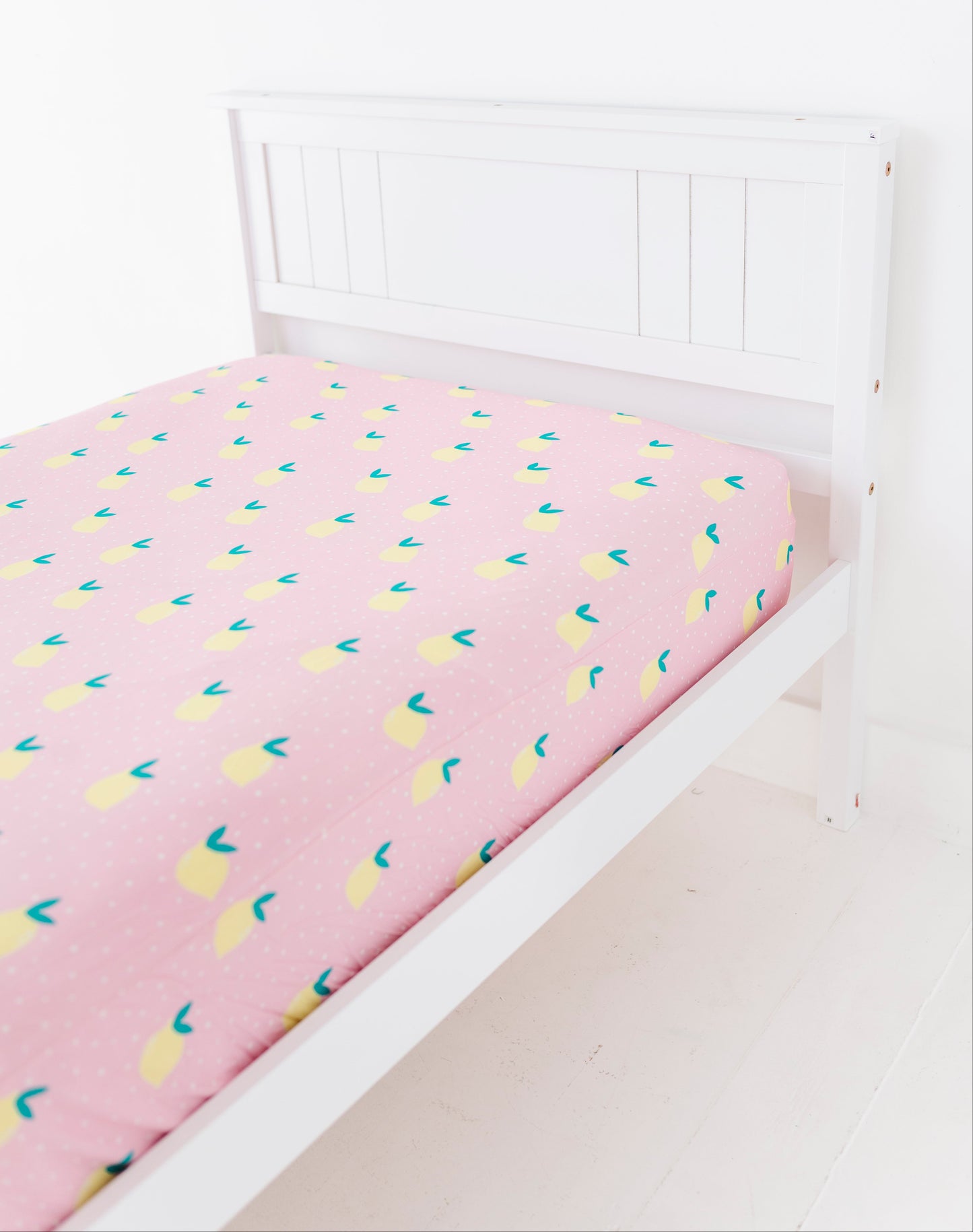 Pink bed sheet with lemon patterns on a white bedframe
