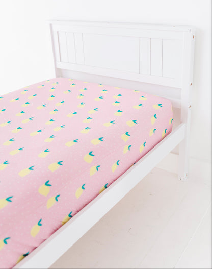 Pink bed sheet with lemon patterns on a white bedframe