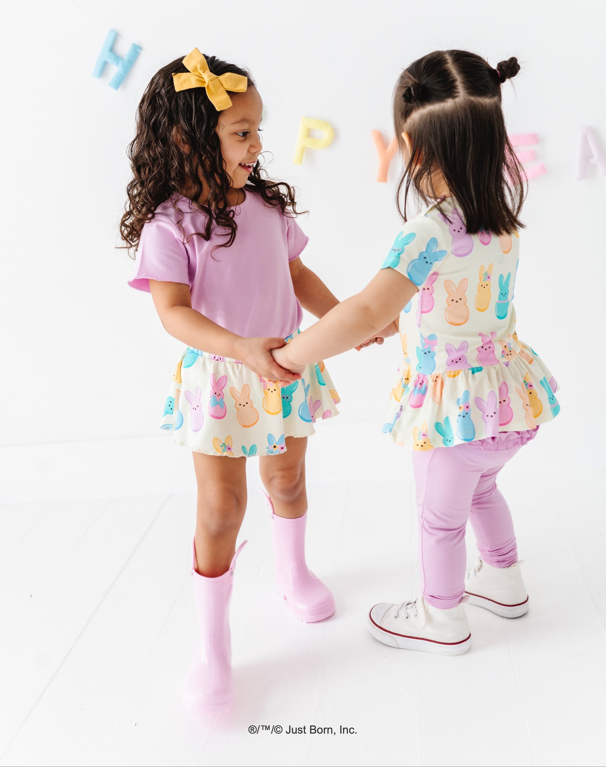 Two young girls in colorful outfits standing on a white background