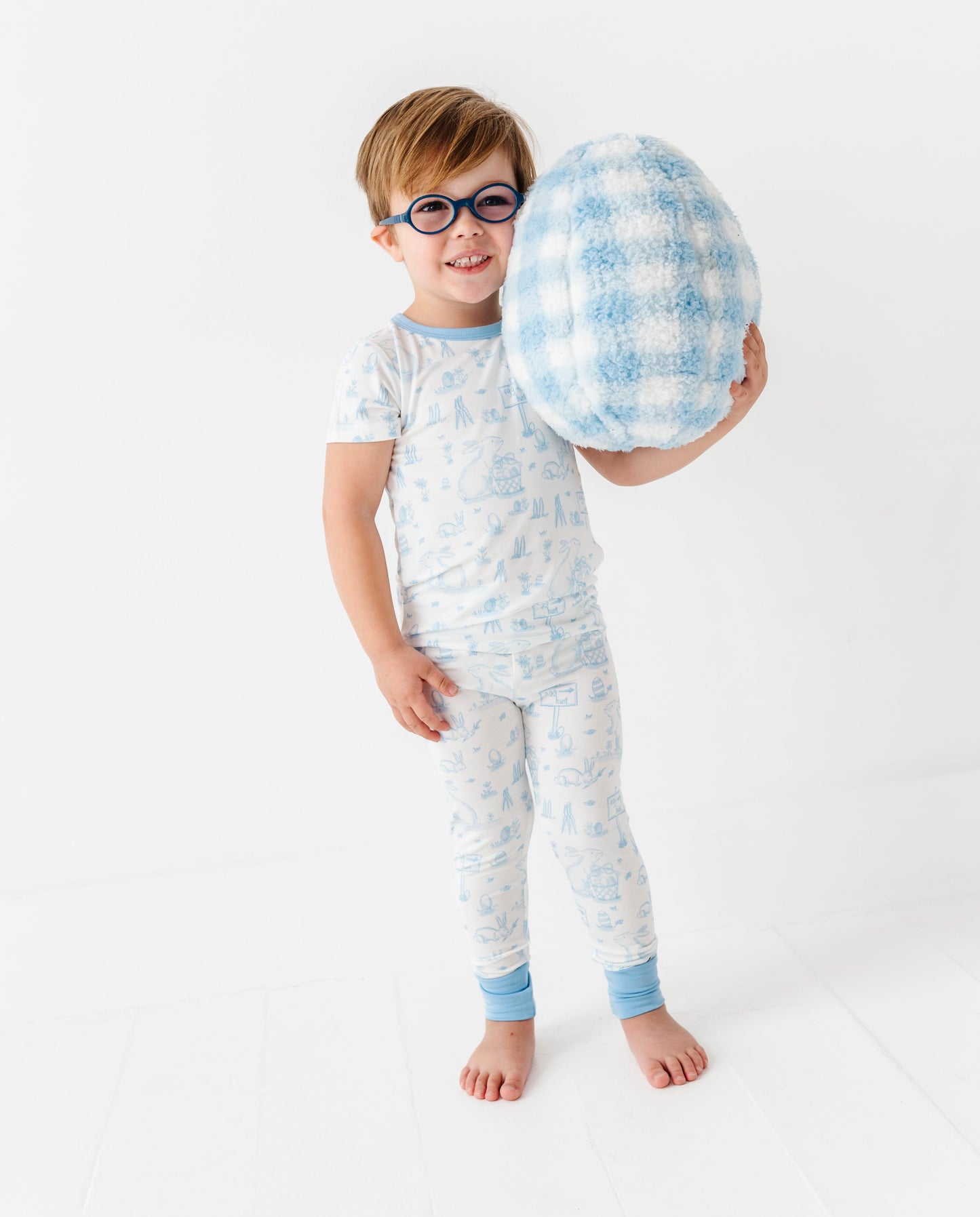 Child wearing a light blue bamboo pajama set holding a checkered pillow on a white background