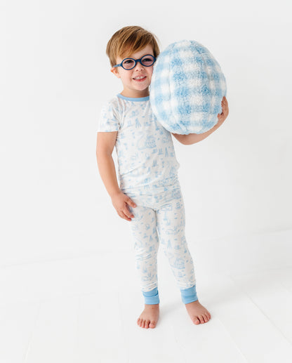 Child wearing a light blue bamboo pajama set holding a checkered pillow on a white background