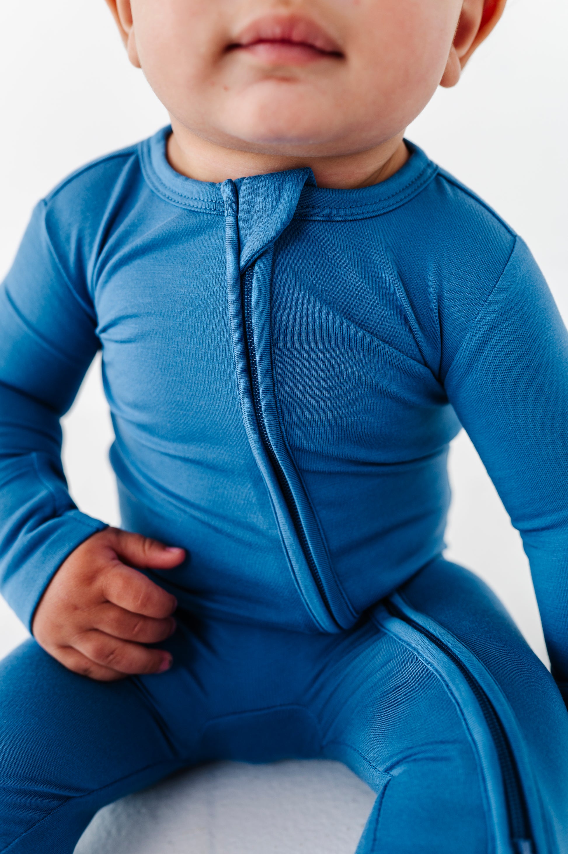 Child wearing a blue bamboo zip romper outfit on a white background
