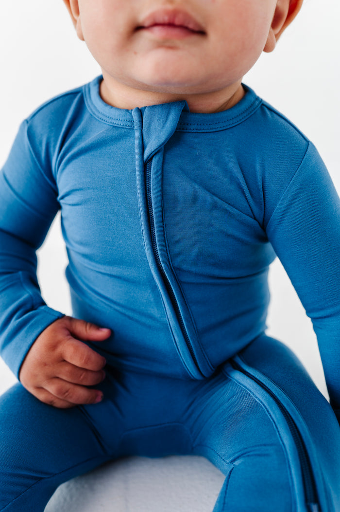 Child wearing a blue bamboo zip romper outfit on a white background