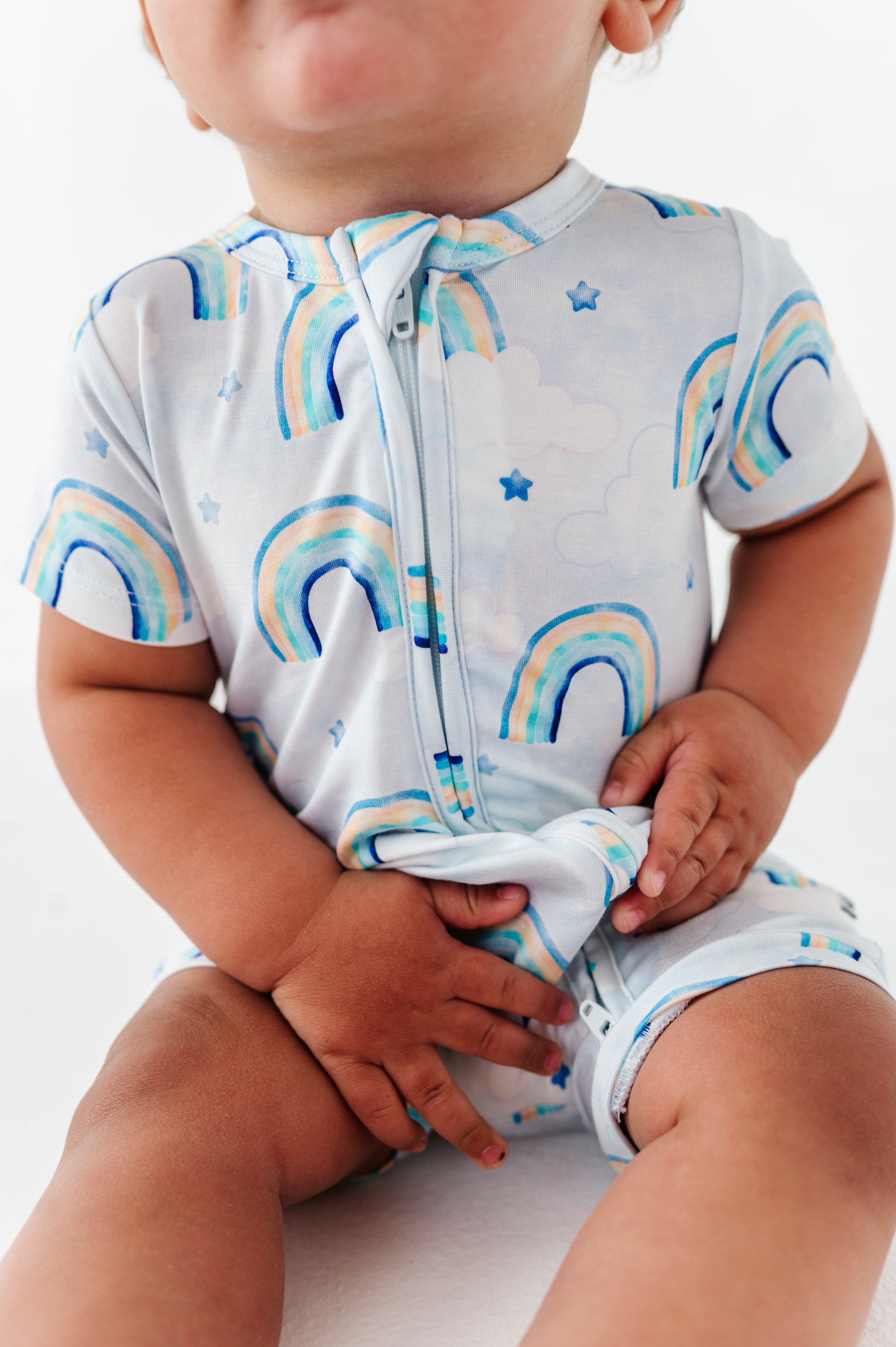 Baby wearing a watercolor rainbow-patterned bamboo romper on a white background
