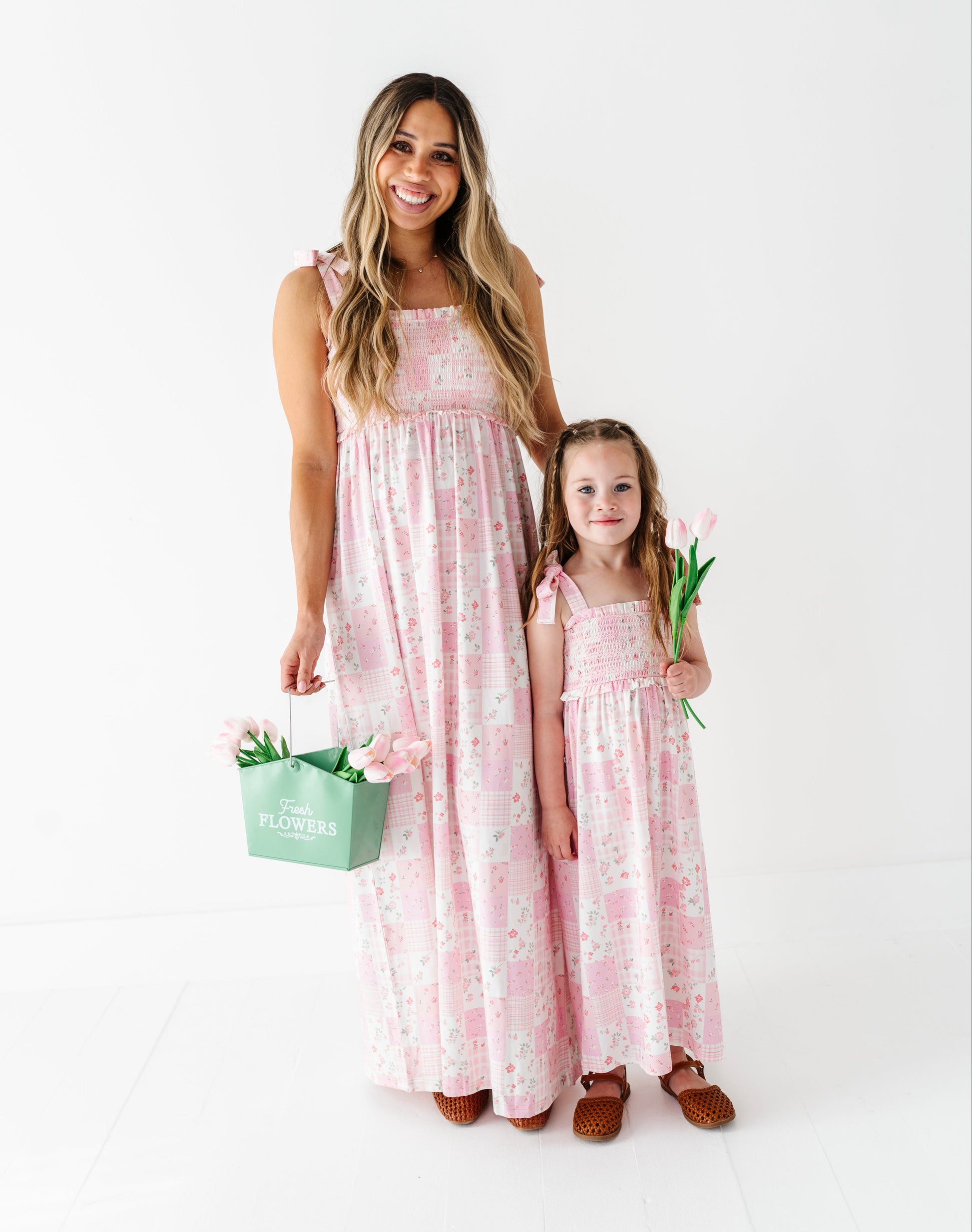 Woman and child in matching pink floral bamboo dresses holding flowers on a white background