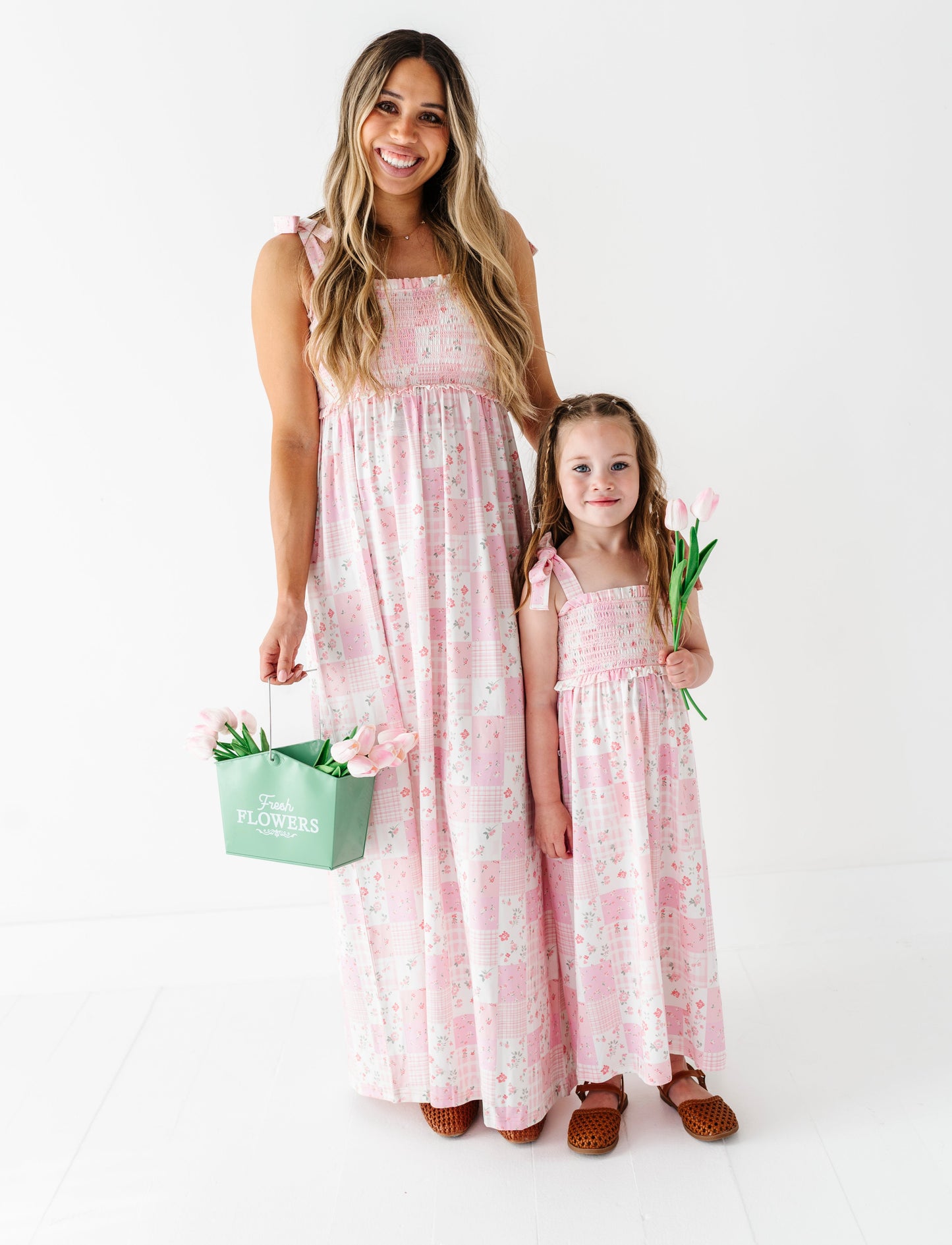 Woman and child in matching pink floral bamboo maxi dresses holding flowers on a white background