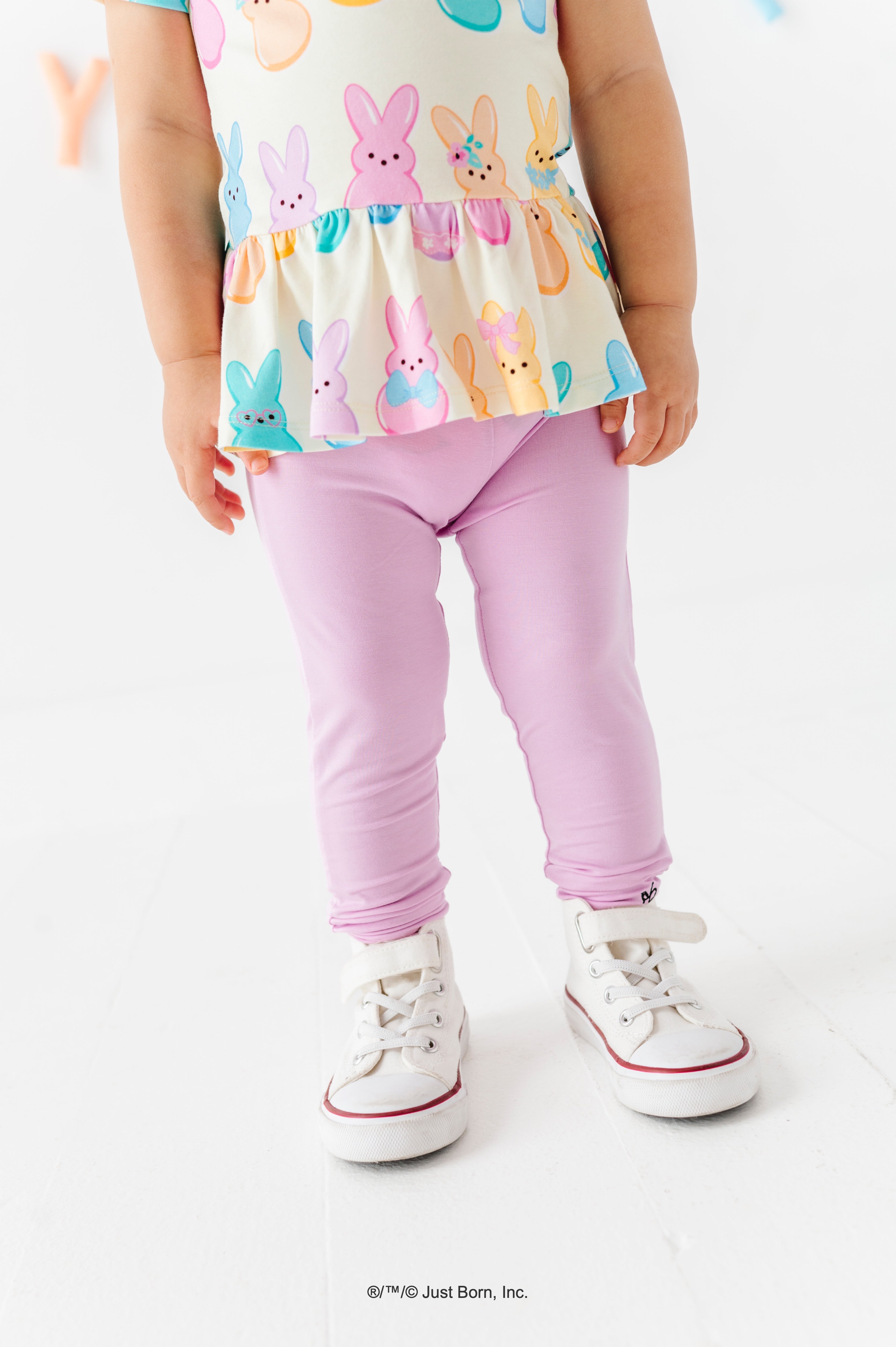 Child wearing a colorful PEEPS® peplum top with lavender leggings and white sneakers on a white background
