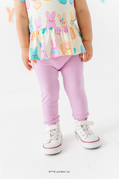 Child wearing a colorful PEEPS® peplum top with lavender leggings and white sneakers on a white background