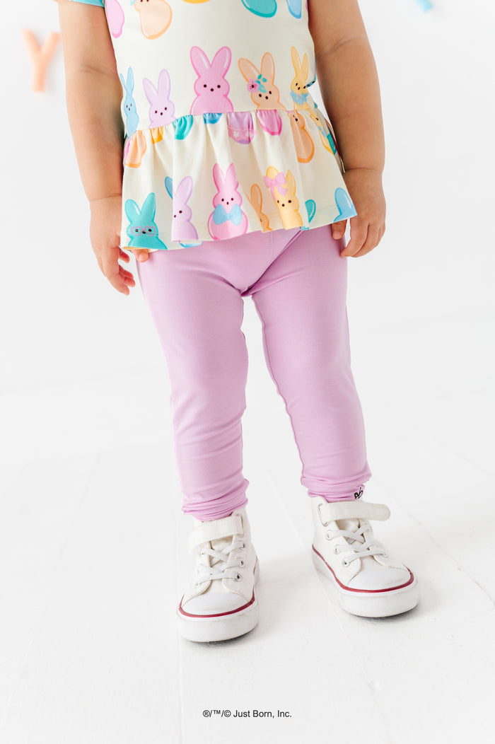 Child wearing a colorful PEEPS® peplum top with lavender leggings and white sneakers on a white background