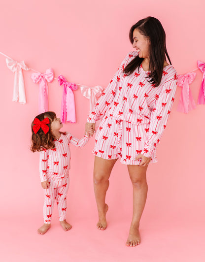 Mother and daughter wearing matching red bow bamboo pajamas on a pink background