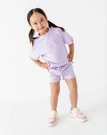 Young girl wearing a purple outfit with white sneakers on a white background