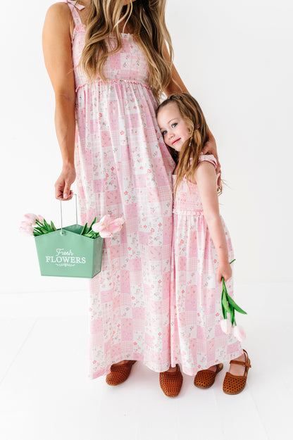 Mama and mini in matching pink floral bamboo dresses holding a green 'Flowers' bag on a white background