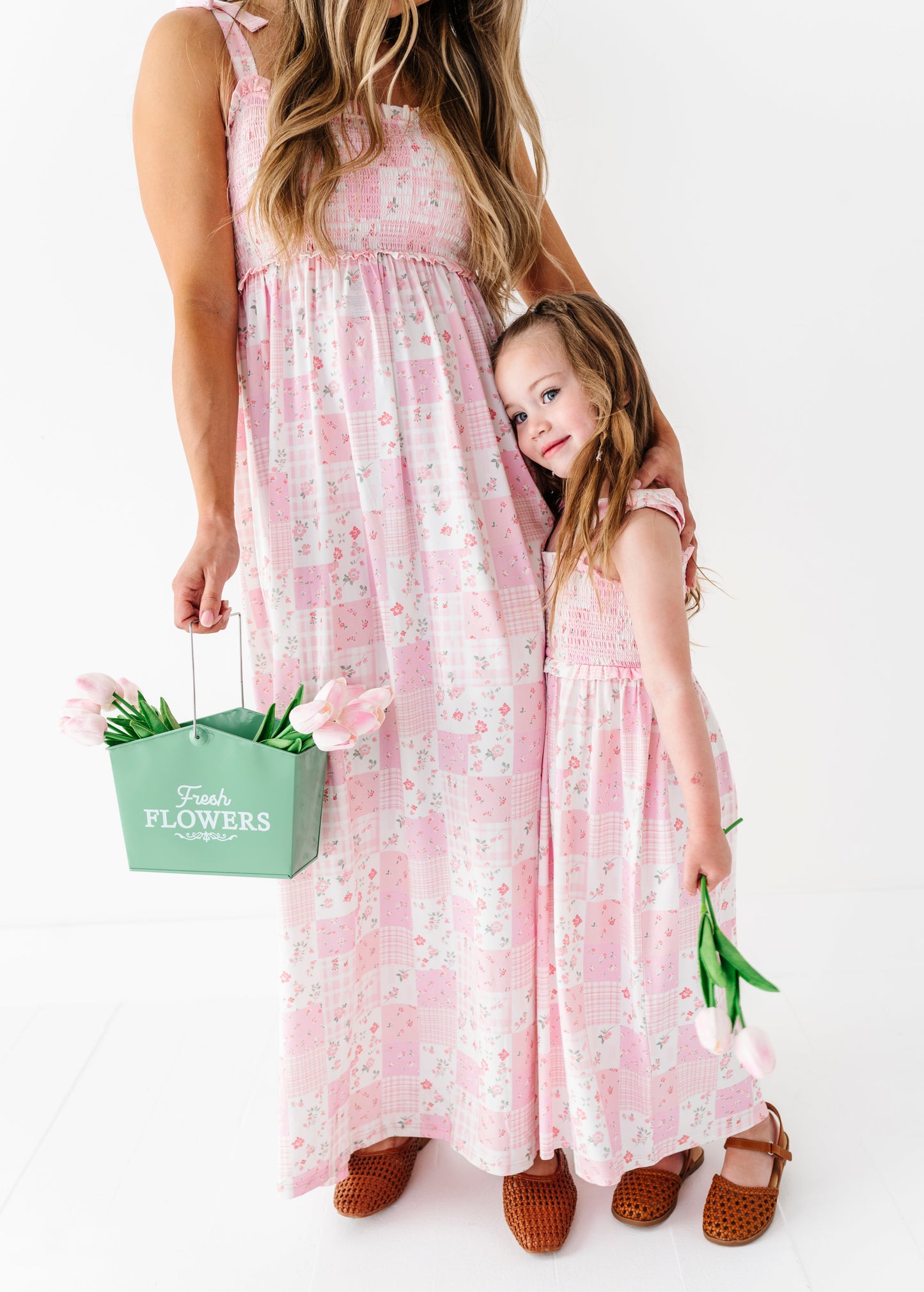 Two people in matching pink floral bamboo maxi dresses holding a green 'Flowers' bag on a white background