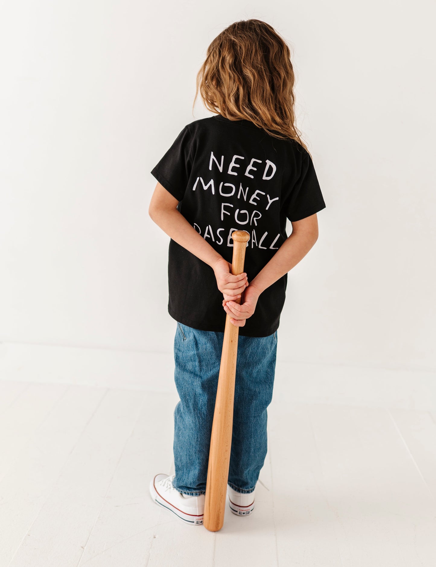 Child wearing a black t-shirt with text holding a baseball bat on a white background