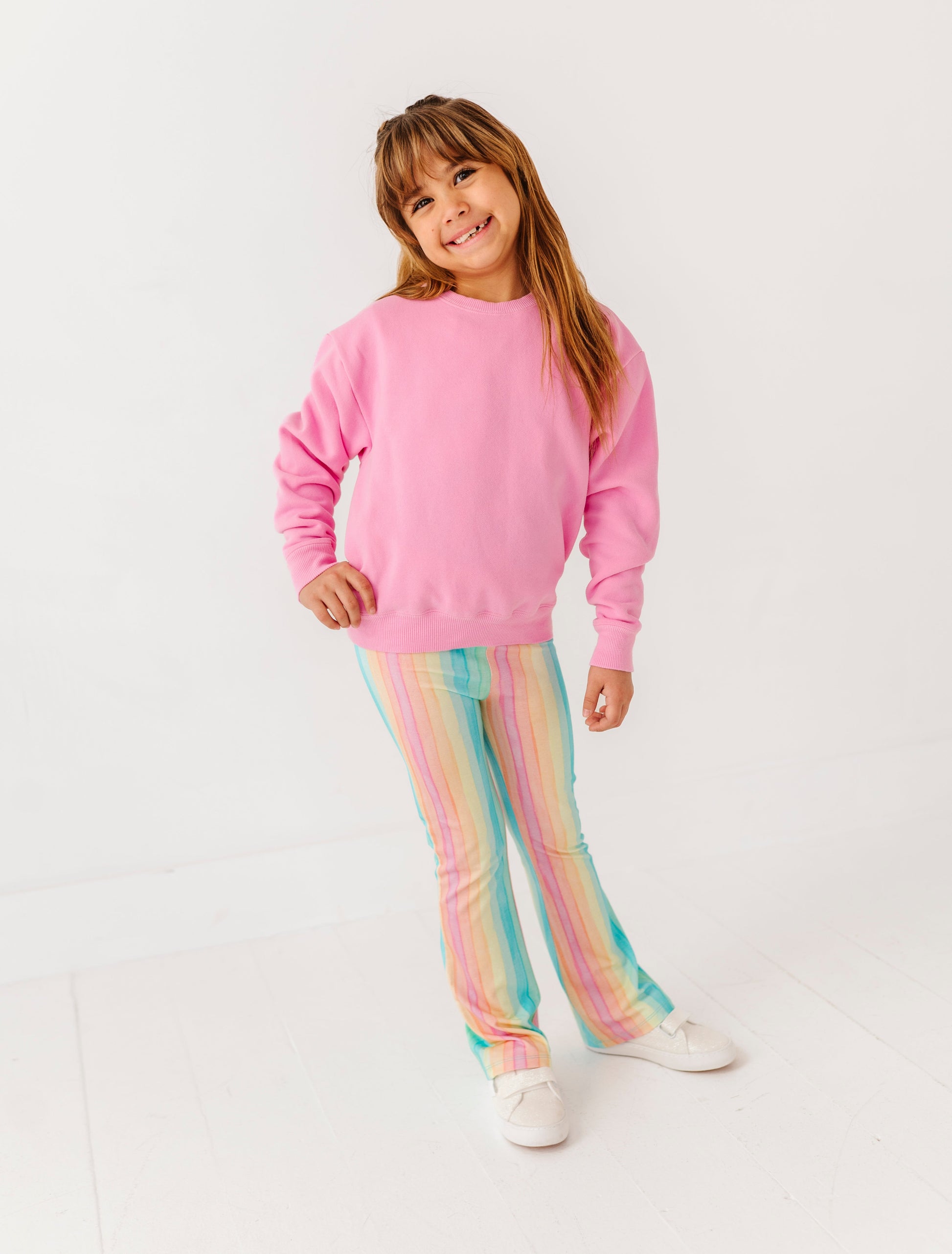 Young girl wearing a pink sweatshirt and colorful striped pants on a white background