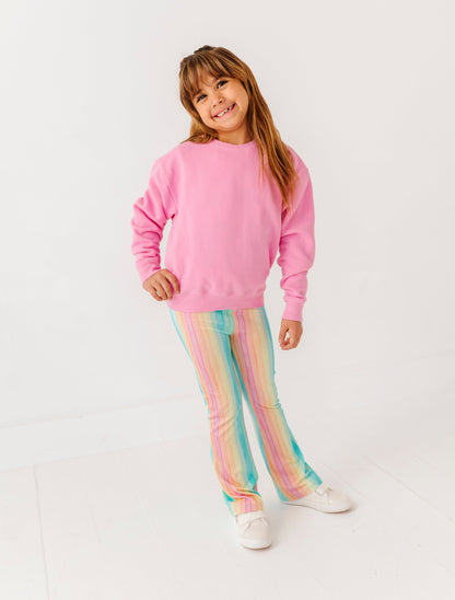 Young girl wearing a pink sweatshirt and colorful striped pants on a white background