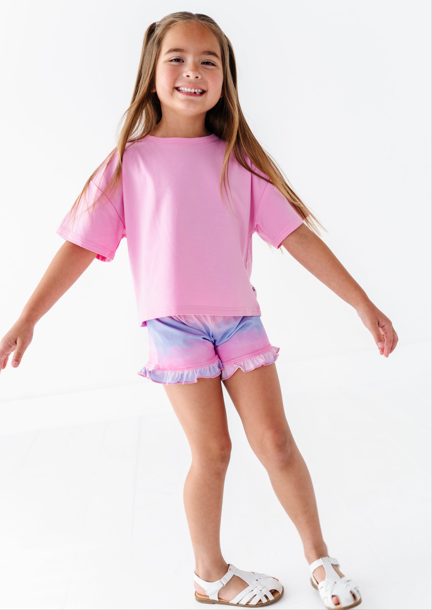 Young girl wearing a pink bamboo-cotton top and colorful bamboo biker shorts on a white background