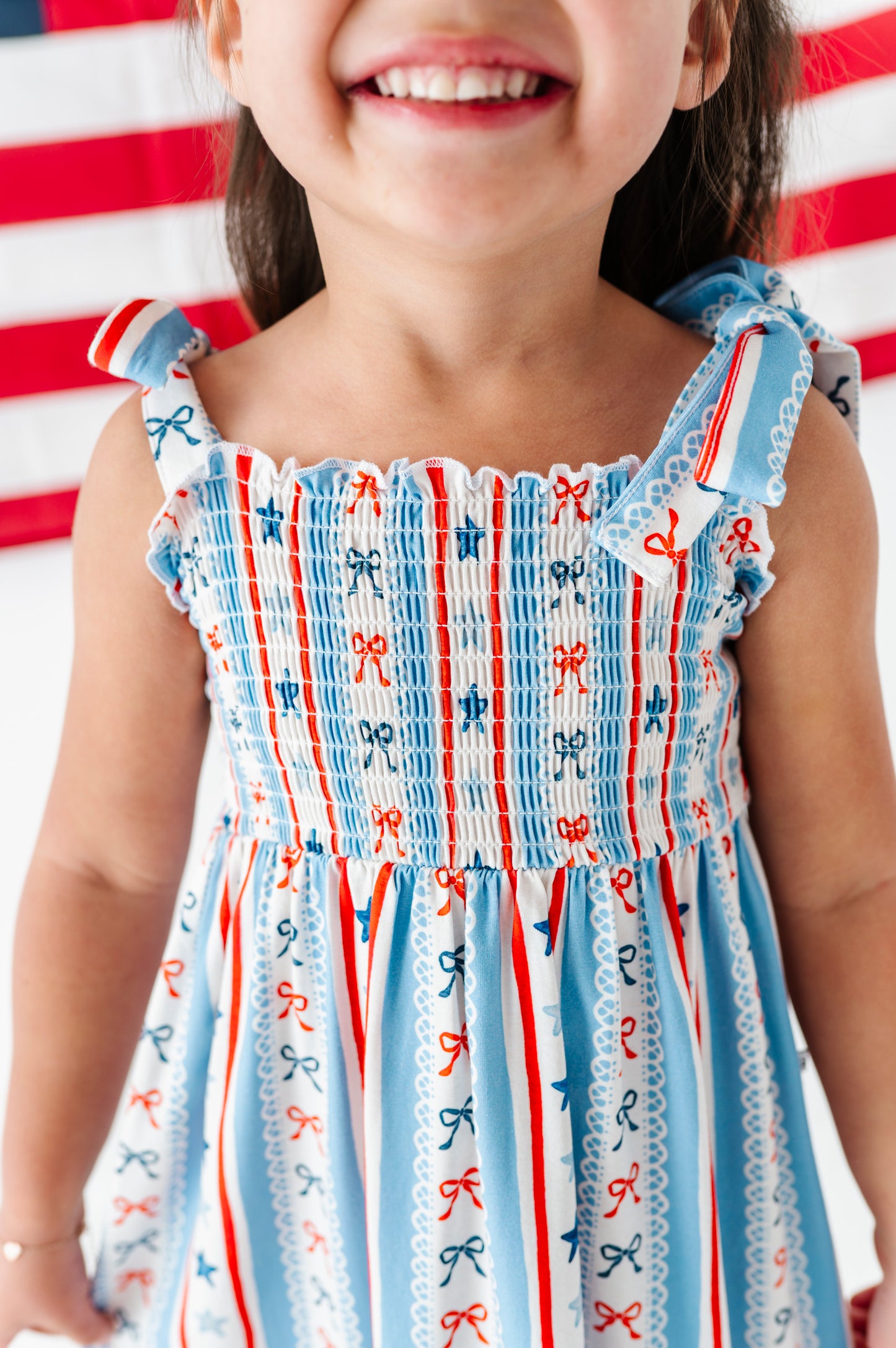 Child wearing a dress with red, white, and blue patterns against an American flag background