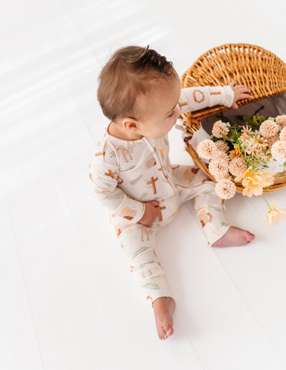 Baby in a patterned bamboo Easter outfit sitting next to a wicker basket with flowers on a white background