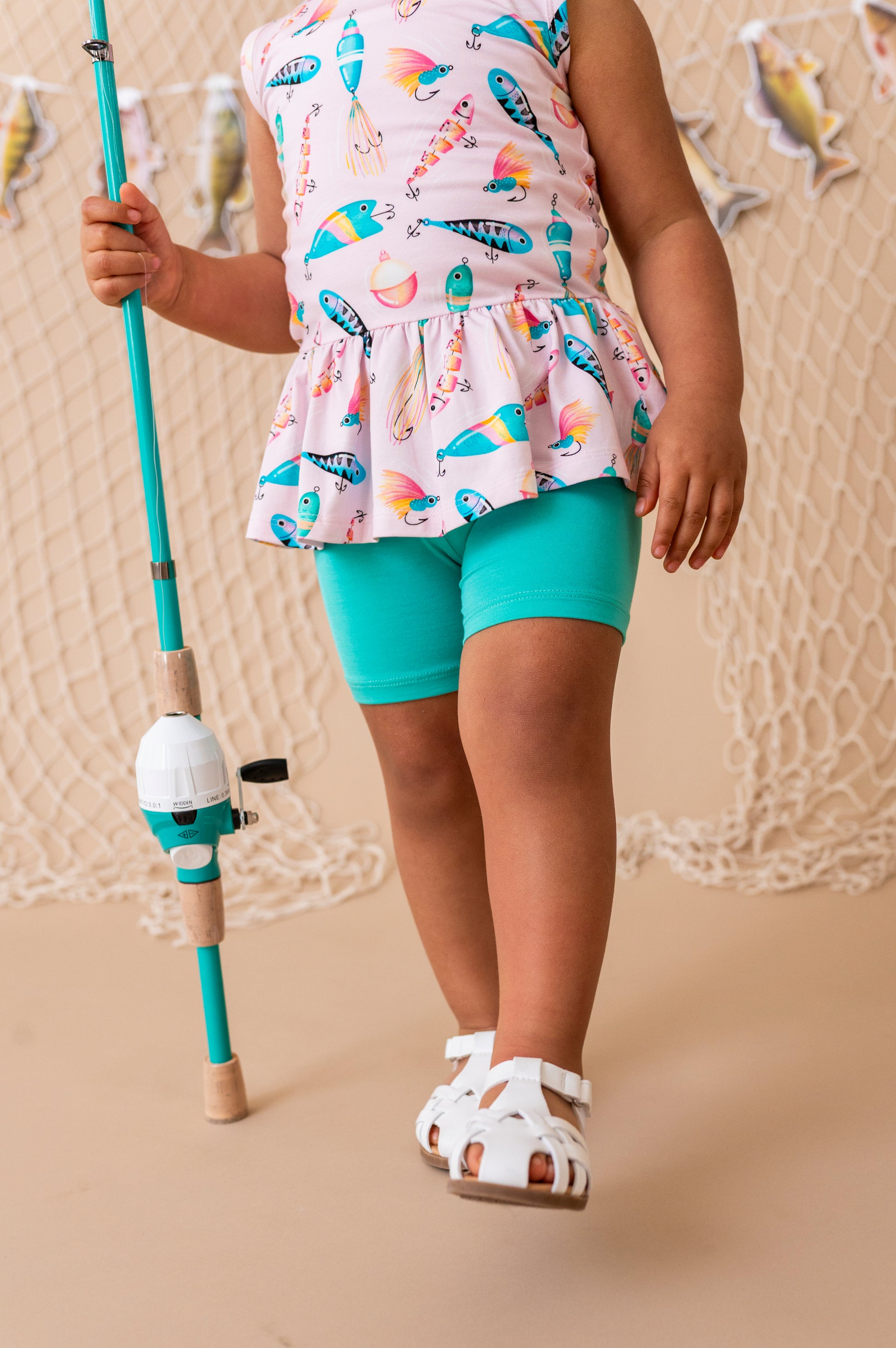 Child wearing a colorful sleeveless top and turquoise shorts, holding a fishing rod.
