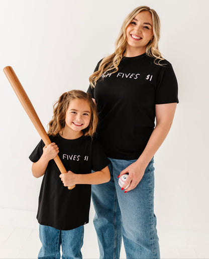 Woman and child wearing matching black t-shirts with text, holding a baseball bat and ball.